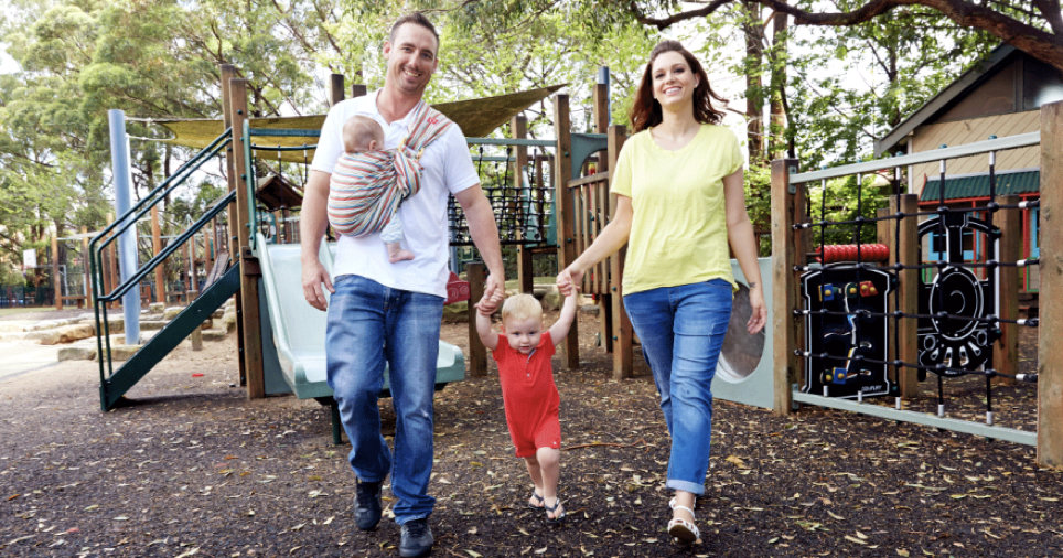 Dad carrying new born in a baby carrier with family in a playground