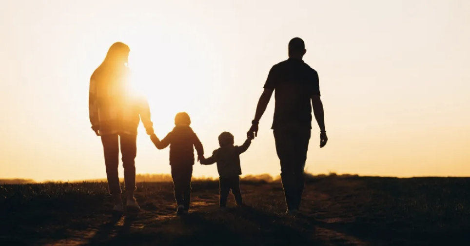 family of four holding hands and walking towards a sunset