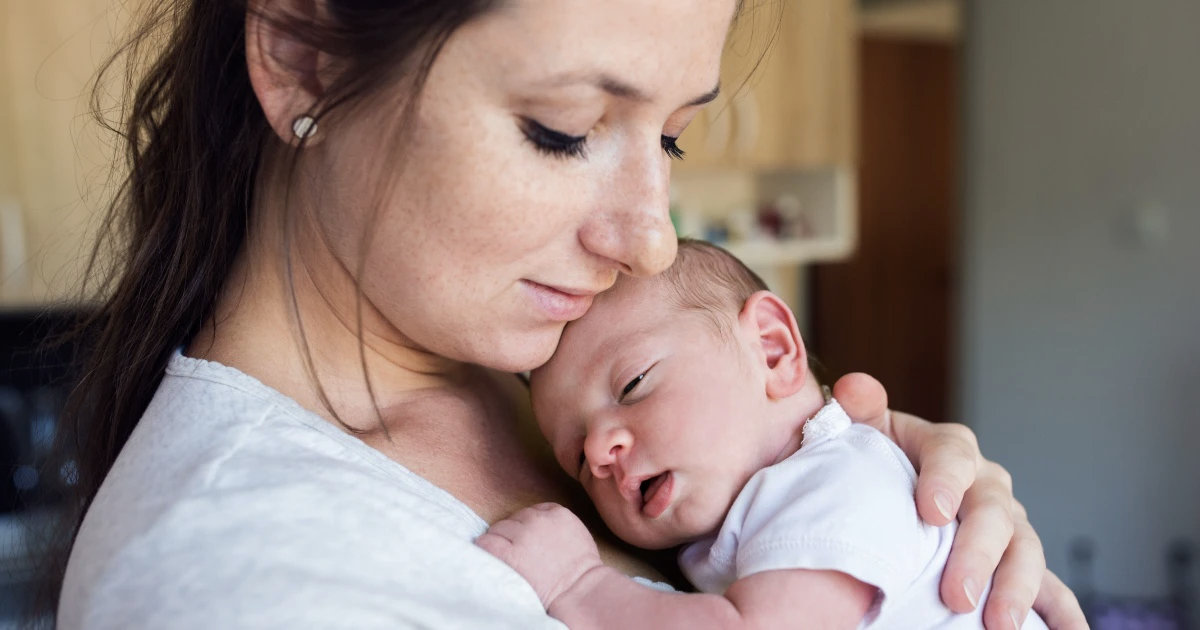 Mother in a white tee shirt holding her new born on her chest