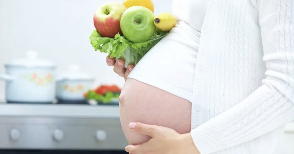 Pregnant mum holding belly in one hand and holding fruit in the other