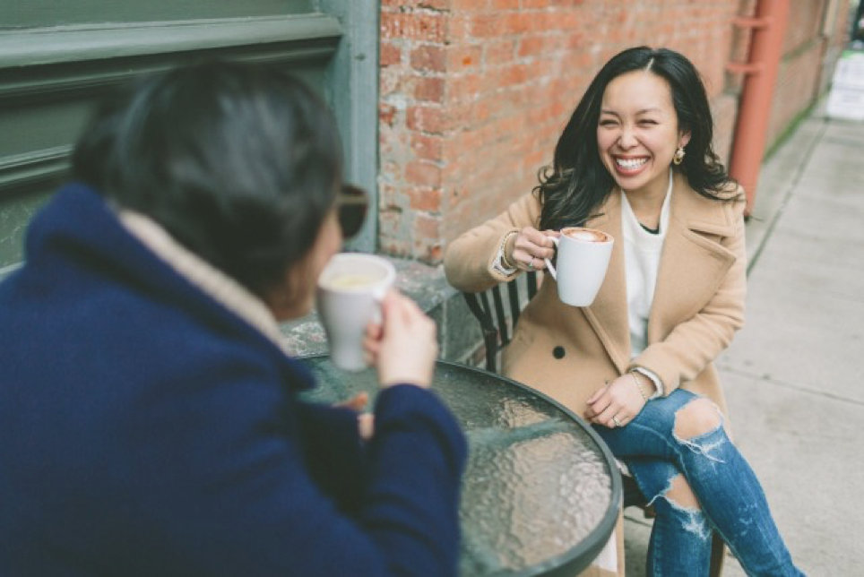 two women drinking a coffee at a cafe outside